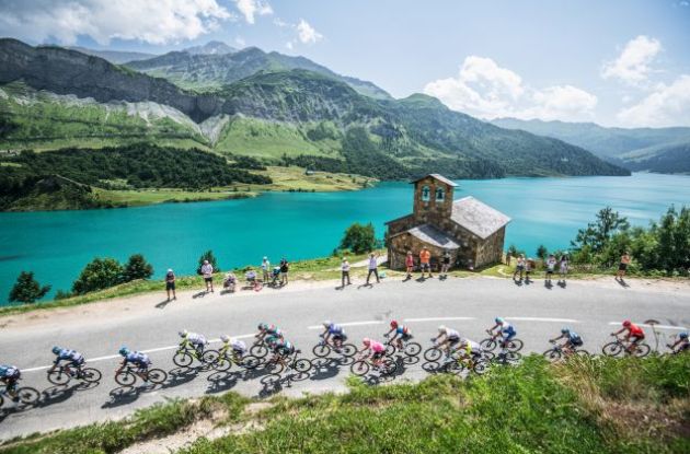 Tour de France cyclists riding past beautiful lake in Alps