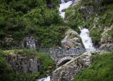 Cyclists passing waterfall and crossing bridge in French mountains 