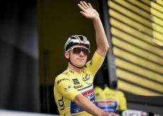 Remco Evenepoel waving from the podium wearing the yellow jersey